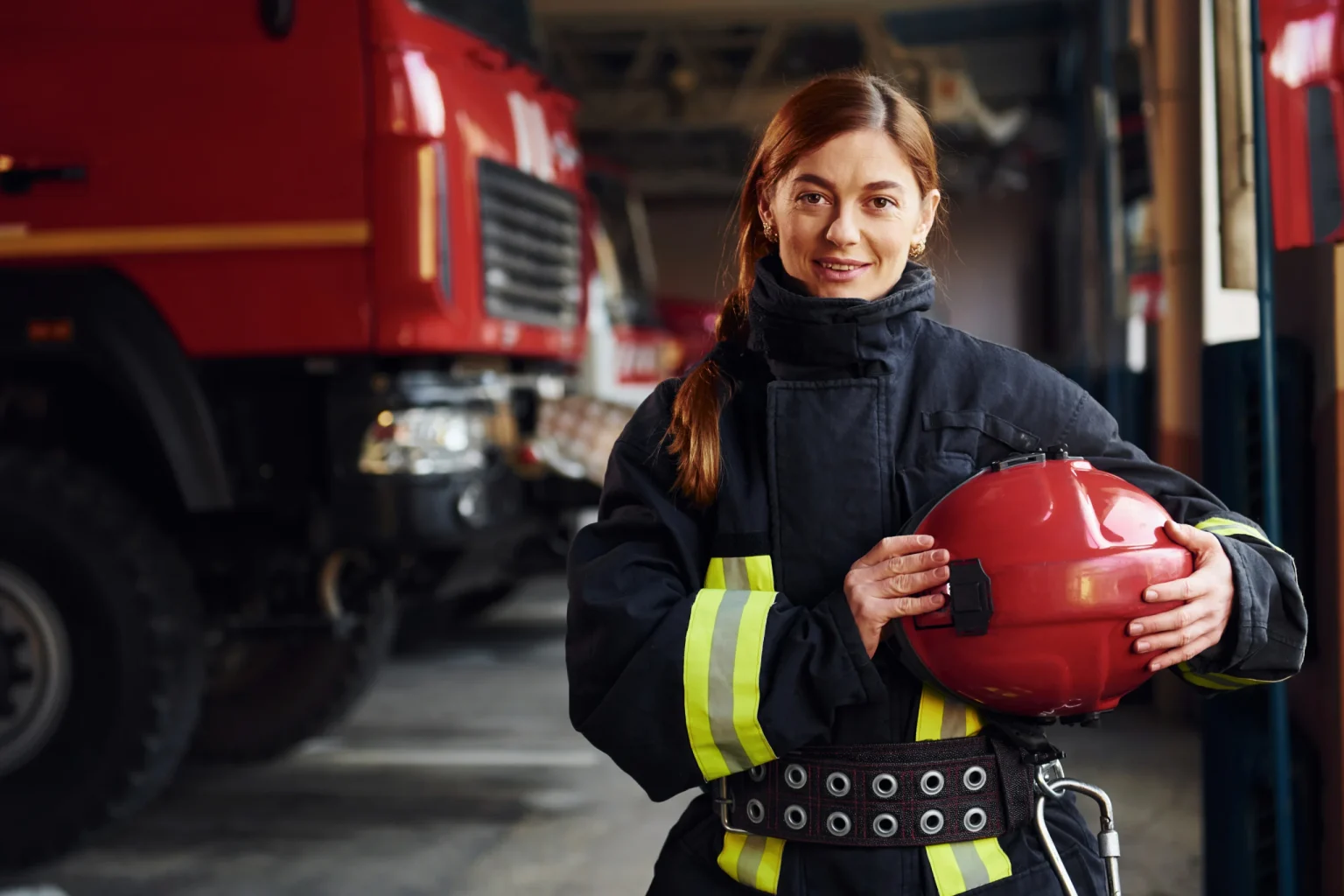 Smiling firefighter holding a helmet at the station